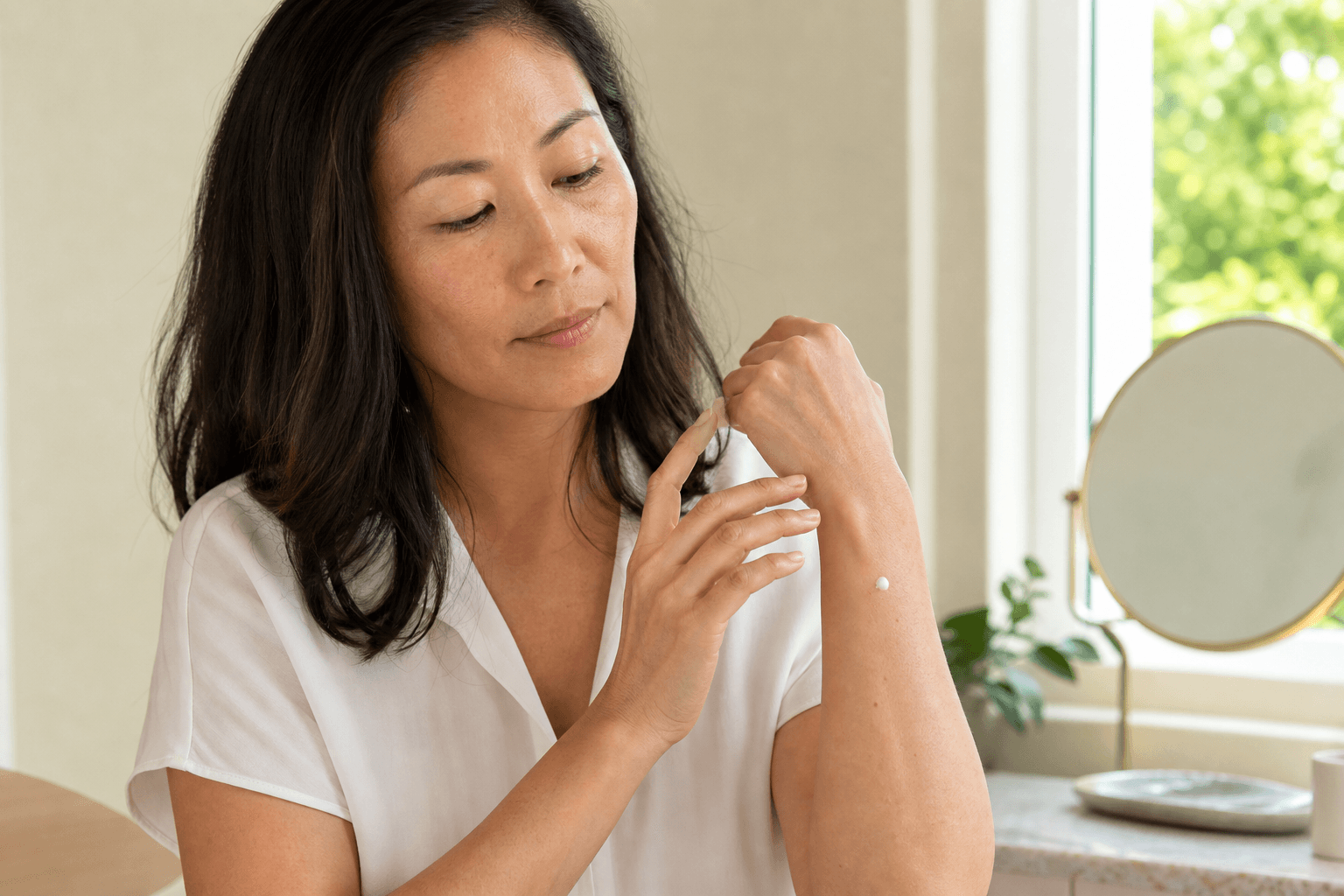 Woman testing a small dot of skin-care cream on her inner forearm in natural window light